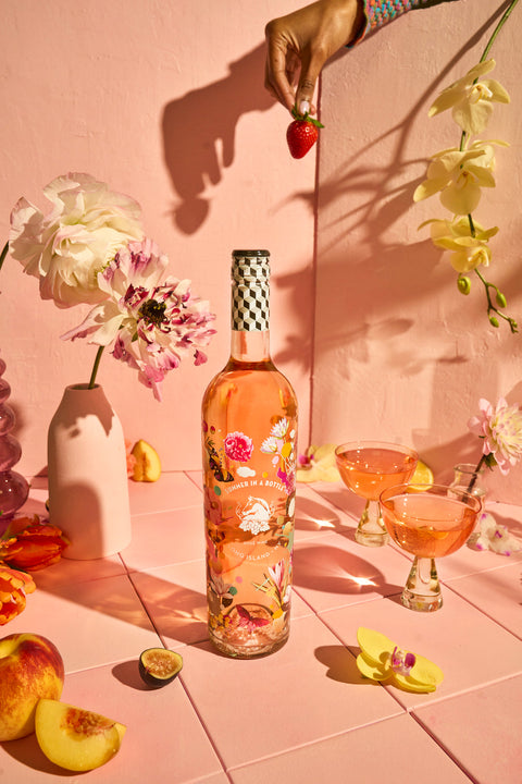 Bottle of pink floral wine on a pink surface with flowers and fruit